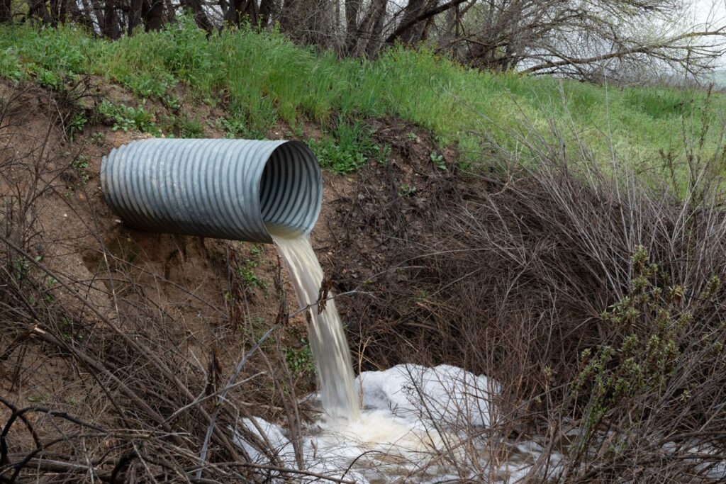 The Art of Drawing Readers In: Your attractive post title goes here A rural drainage pipe pouring water into a natural ravine, surrounded by green vegetation.